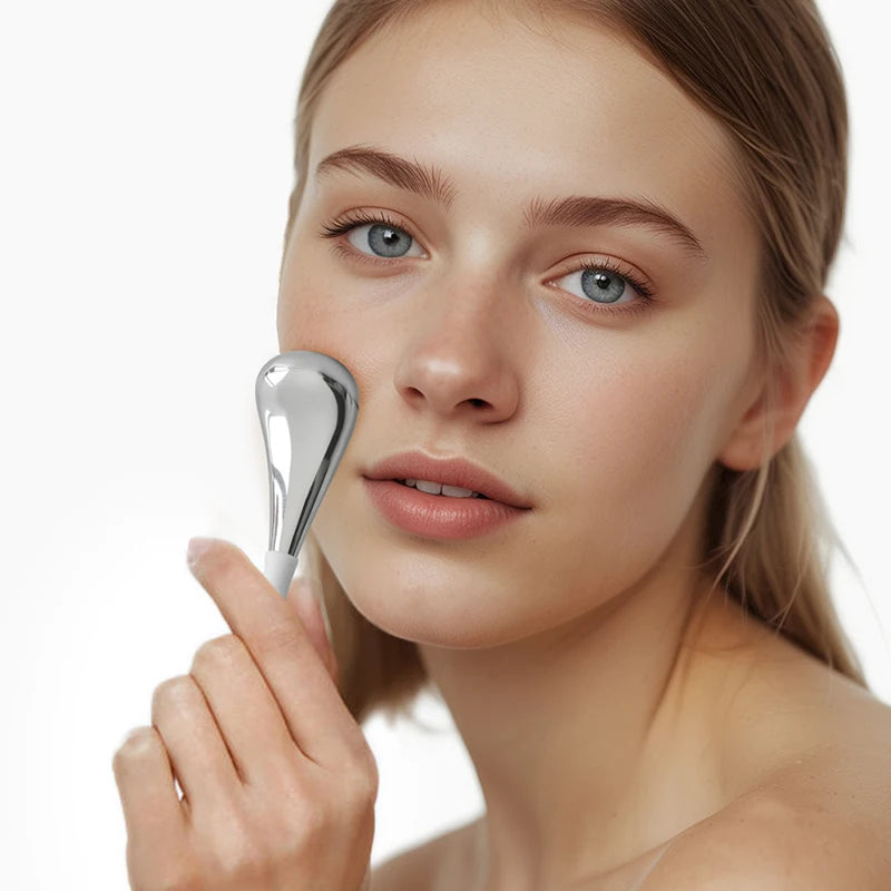 Woman using a silver facial roller on her face against a white background